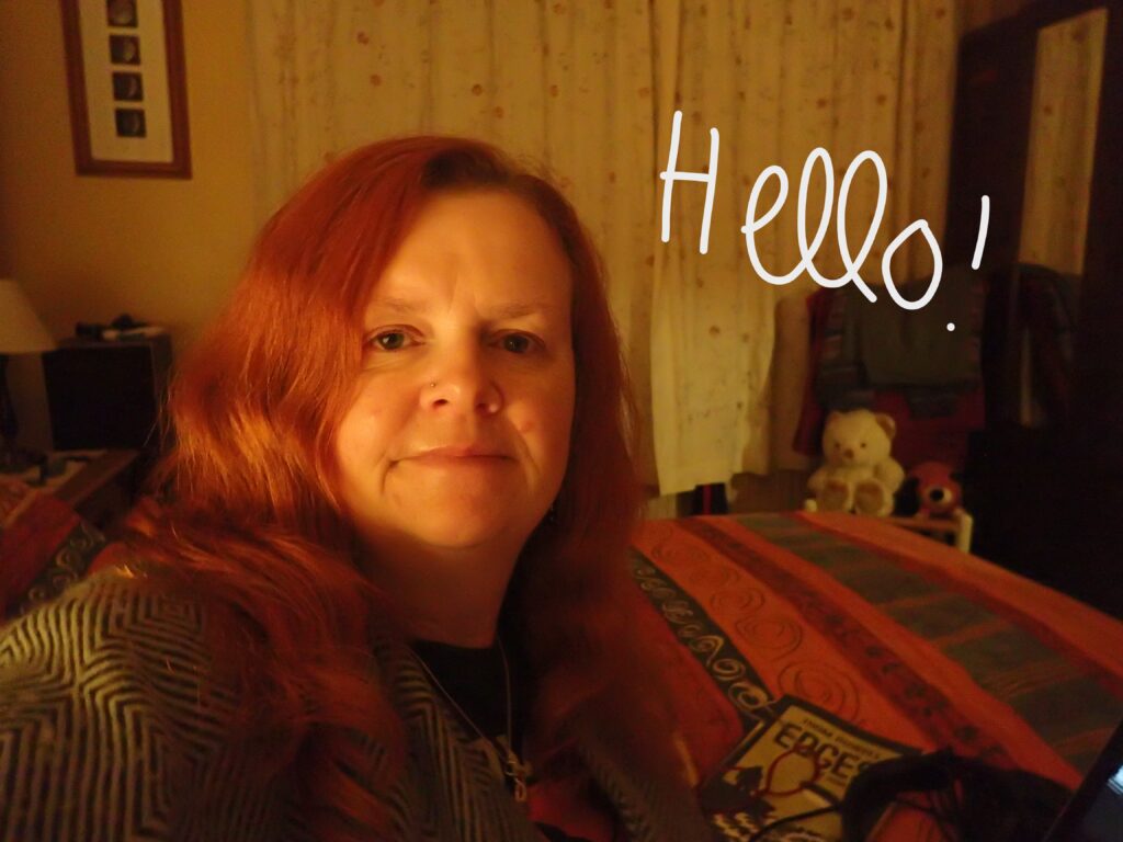 A red haired woman sat in a bedroom in the glow of lamp light late at night.