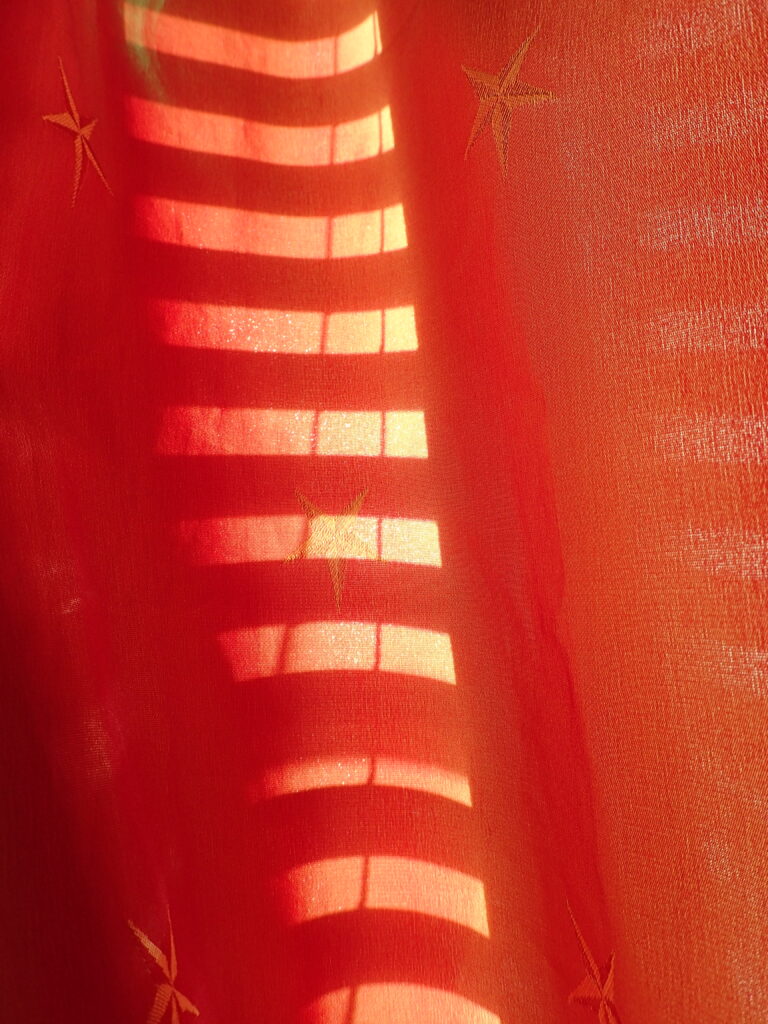 Horizontal rays of light upon an orange curtain.