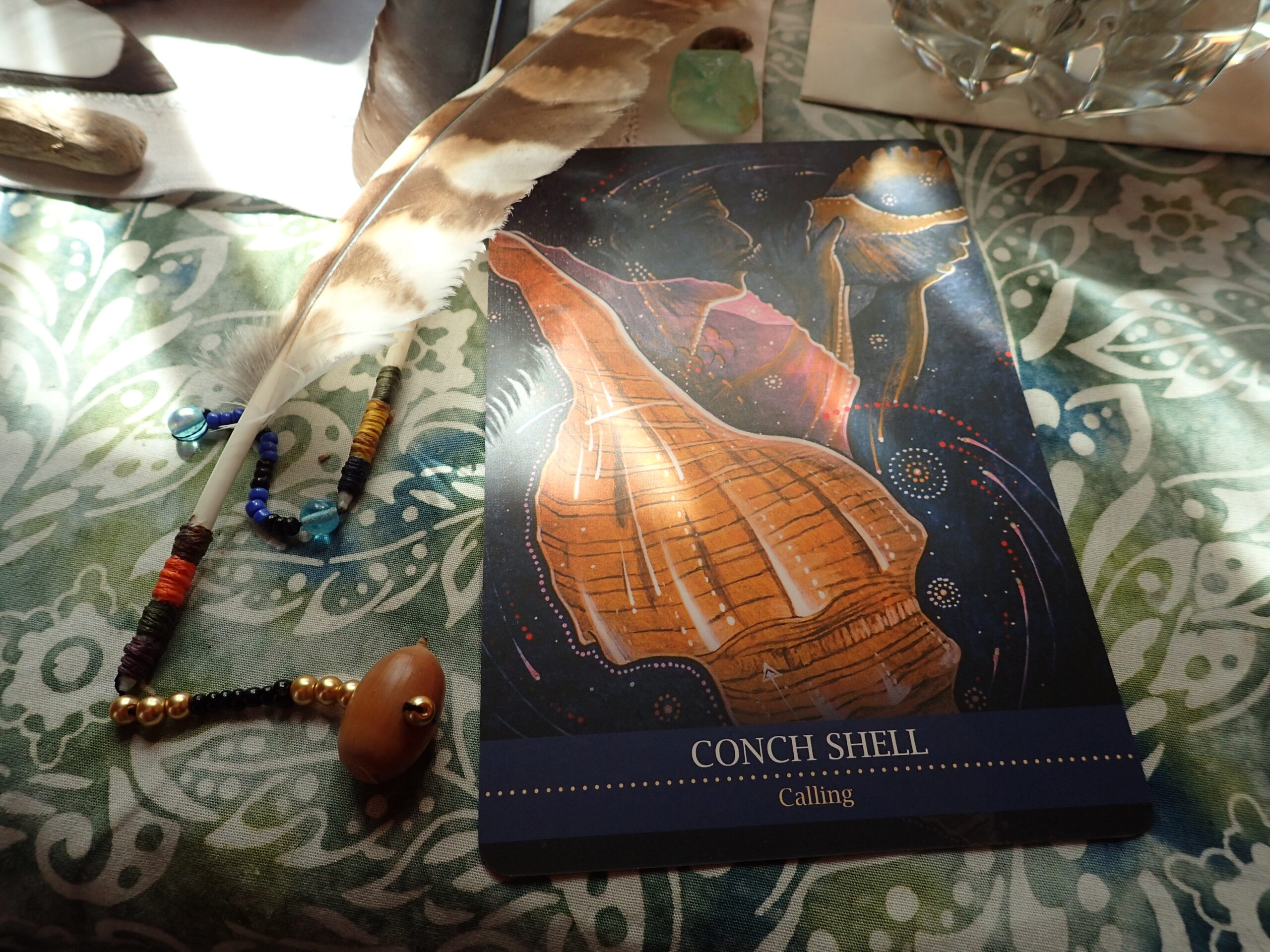 An owl feather next to a oracle card which says conch shell, calling.
